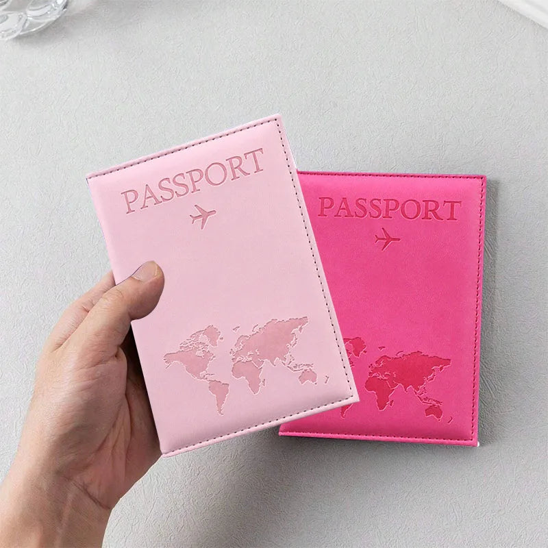 A hand holds a pink passport holder with a world map design on the cover.