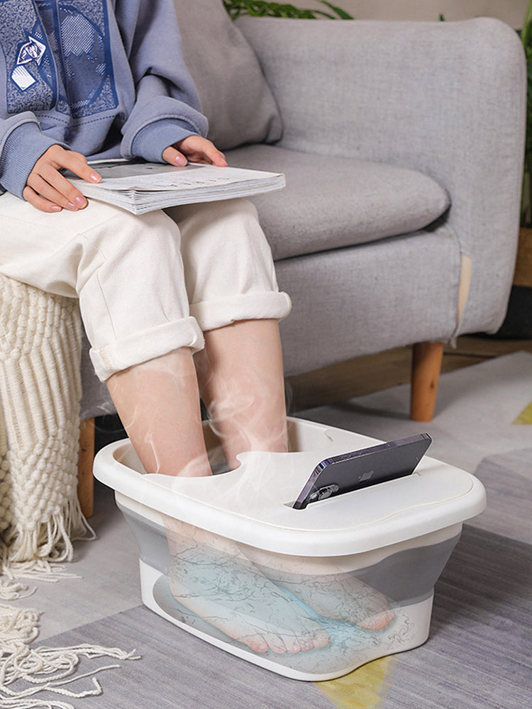 Una persona relajándose con un cubo de baño y pies plegable que reposa en el suelo.