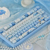 Ocean blue PBT keycaps for mechanical keyboards arranged on a light blue surface with pearl strands.