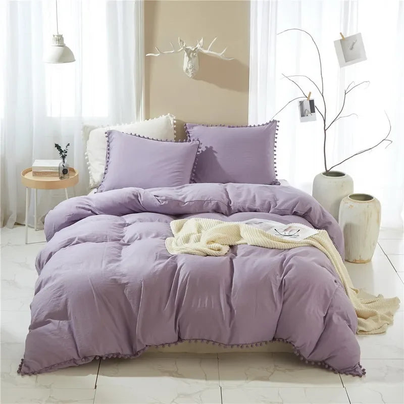 A purple soft washed duvet cover set with pom-pom trim displayed on a bed in a bright room.