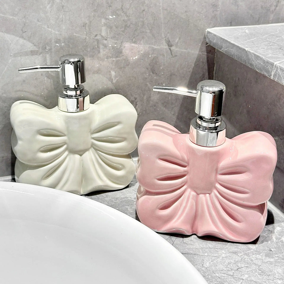 A pink ceramic pump dispenser with a silver pump mechanism sits on a gray countertop next to a white sink.