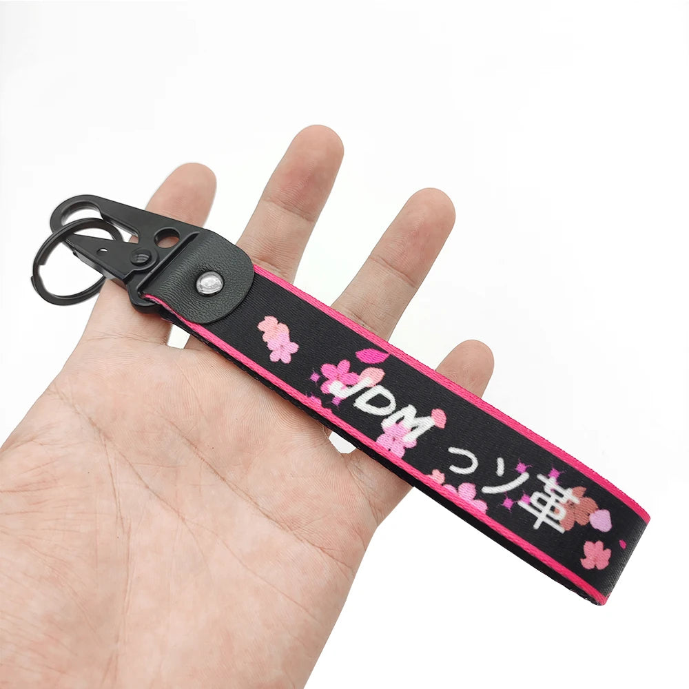A black and pink strap keychain featuring the JDM Eagle beak design held in a hand.
