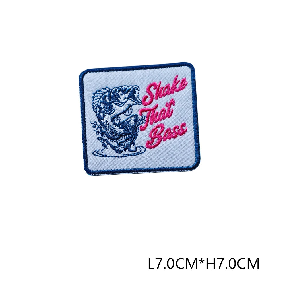 A blue embroidered patch featuring a stylized fish design and the text Shake That Bass in pink thread.