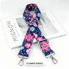 A floral patterned fabric strap in purple and pink is displayed on a white box.