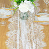Vintage white embroidered floral lace table runner displayed on a wooden table with place settings and a vase of white flower