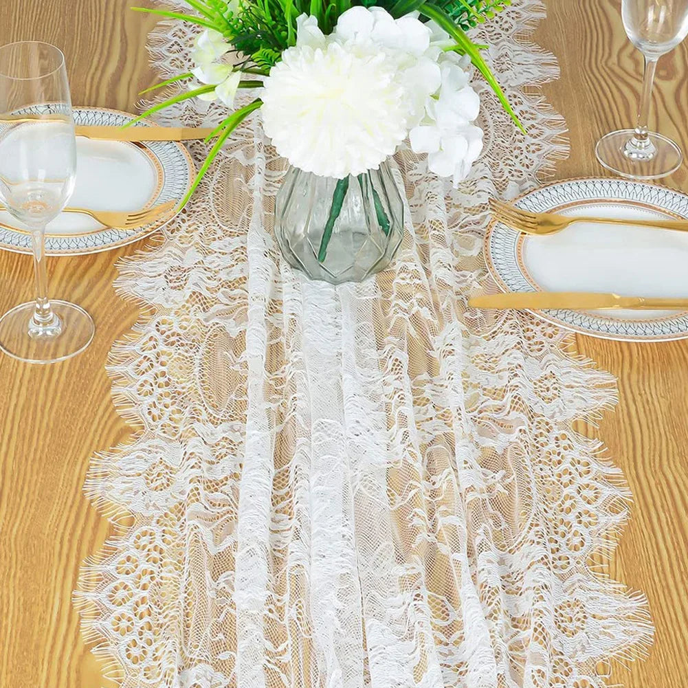 Vintage white embroidered floral lace table runner displayed on a wooden table with place settings and a vase of white flower