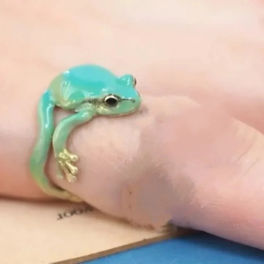 A hand wearing a turquoise green tree frog ring on the finger.