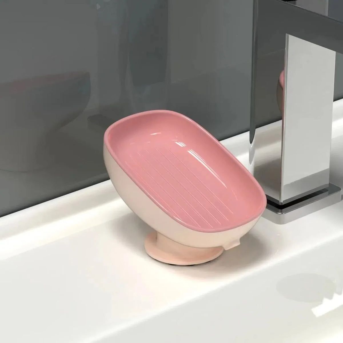 A pink suction cup soap holder with drainage is placed on a white bathroom sink.