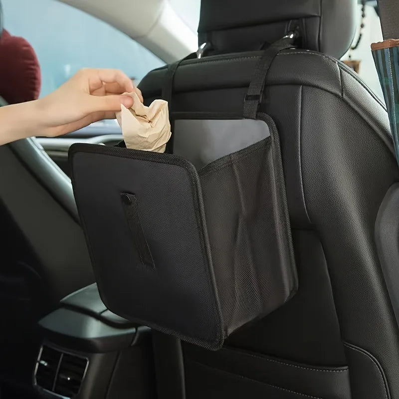 A hand places a tissue into the organizer pocket of a black foldable car trash can and organizer.