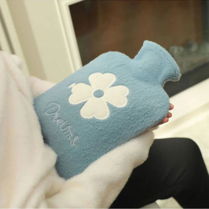 A light blue plush-covered hot water bottle with a white flower design is held in a person's hand.