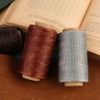 Two spools of waxed polyester thread in copper and gray colors resting on a brown leather surface.