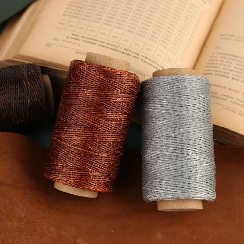 Two spools of waxed polyester thread in copper and gray colors resting on a brown leather surface.