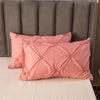 Pink pinch pleated duvet cover set resting on a white bed with a gray upholstered headboard.