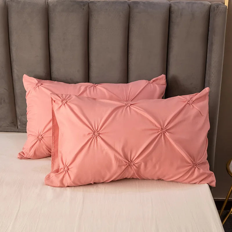 Pink pinch pleated duvet cover set resting on a white bed with a gray upholstered headboard.
