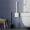 A wall-mounted toilet brush set with a black handle and white silicone head is mounted on a gray tiled wall.
