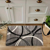 A rectangular rug with a geometric pattern of black and white curved lines on a light wood floor.