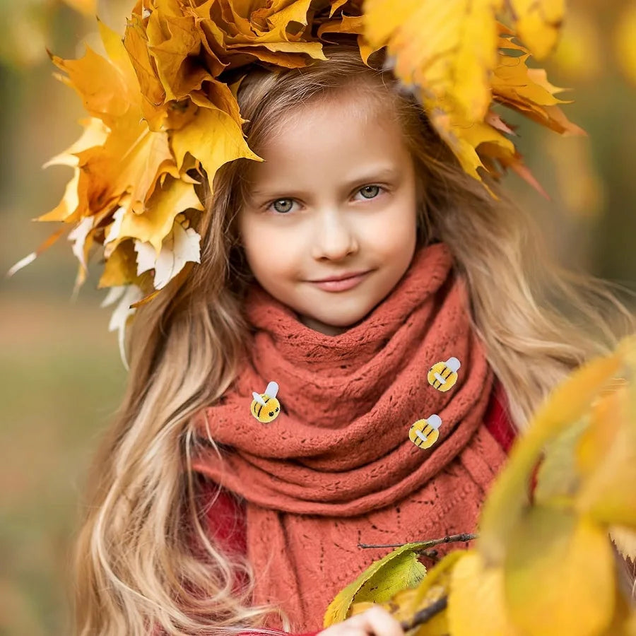 A young girl with long blonde hair wears a crown of yellow autumn leaves and an orange knitted scarf.