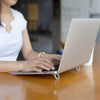A person is using an aluminum portable laptop stand on a wooden table.
