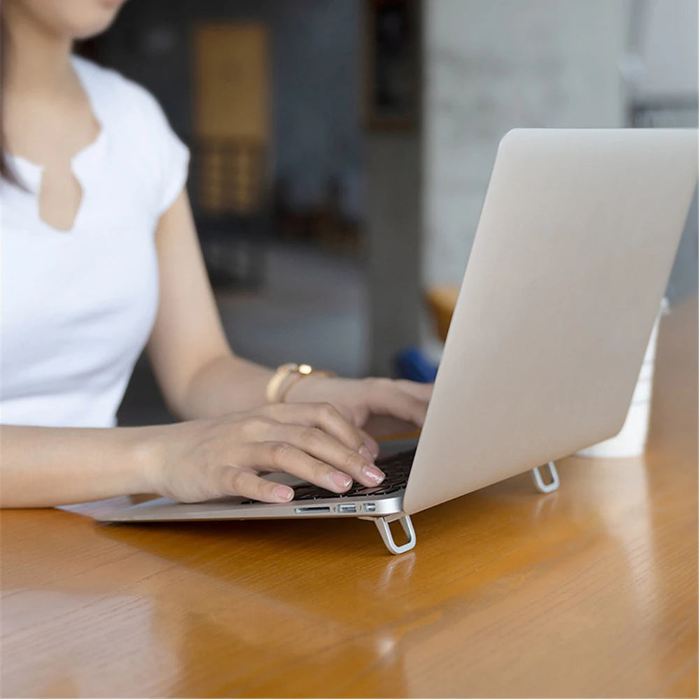 A person is using an aluminum portable laptop stand on a wooden table.