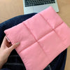 Eine rosafarbene, gesteppte Daunen-Laptoptasche, gehalten von einer Hand, auf einem dunkelblauen Jeanshemd.