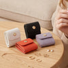 A collection of four compact PU leather jewelry organizer pouches in white, black, orange, and lavender resting on a wooden t