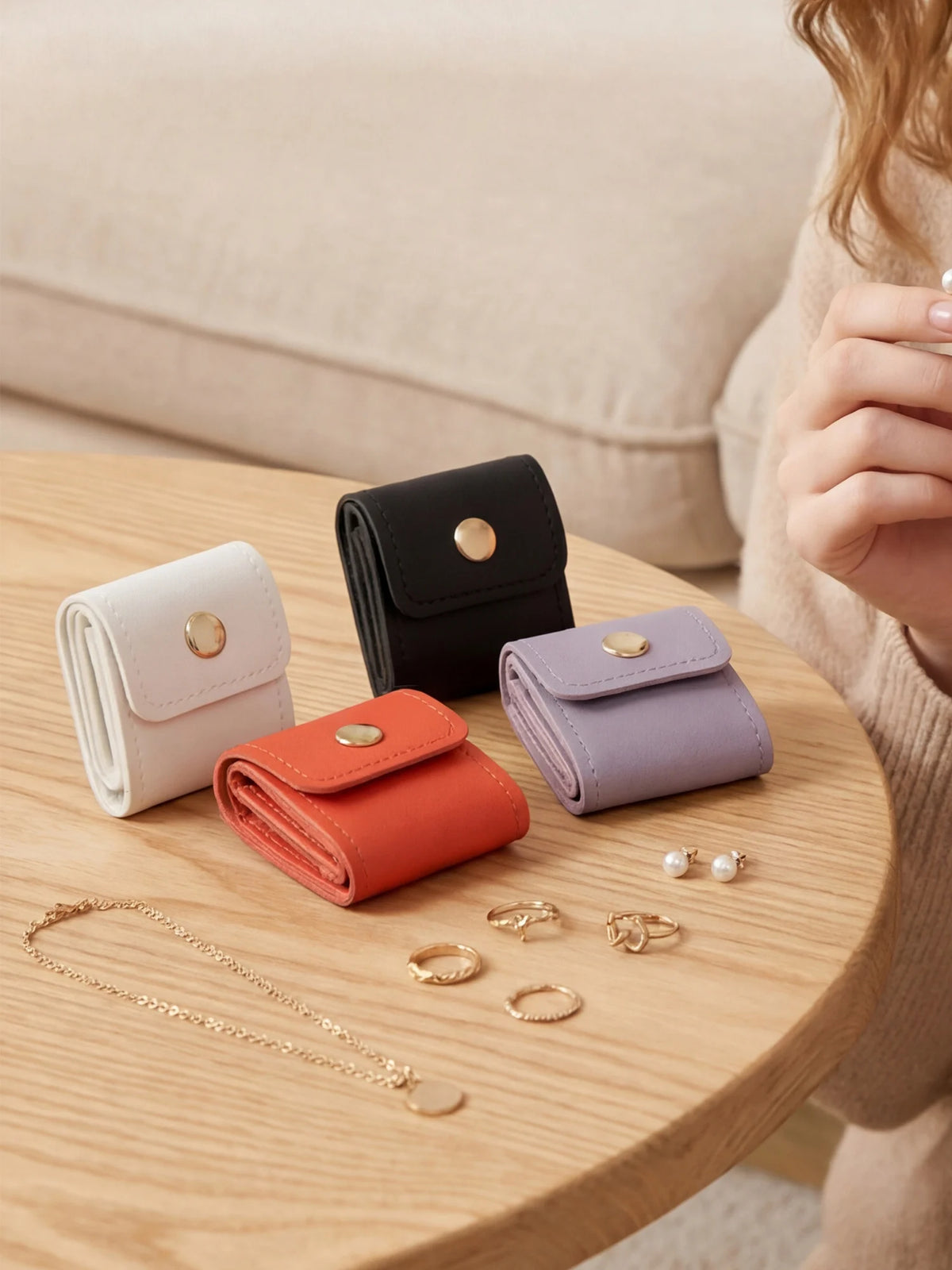 A collection of four compact PU leather jewelry organizer pouches in white, black, orange, and lavender resting on a wooden t