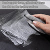 A hand is using a white cleaning sponge to remove dirt from a black leather surface.