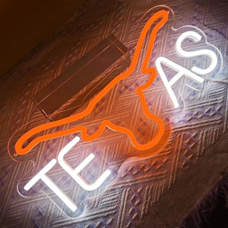 An orange cow head neon sign illuminates a textured surface in a dark room.