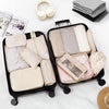 A set of travel packing cubes and storage organizer bags in neutral tones displayed on a white surface.