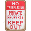 A vintage red and white metal tin sign with the text NO TRESPASSING PRIVATE PROPERTY KEEP OUT.