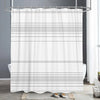 White shower curtain with a black and white geometric pattern hanging from a metal rod in a bathroom setting.