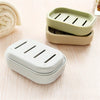 Two compact travel soap holders in light green and white plastic resting on a wooden surface.