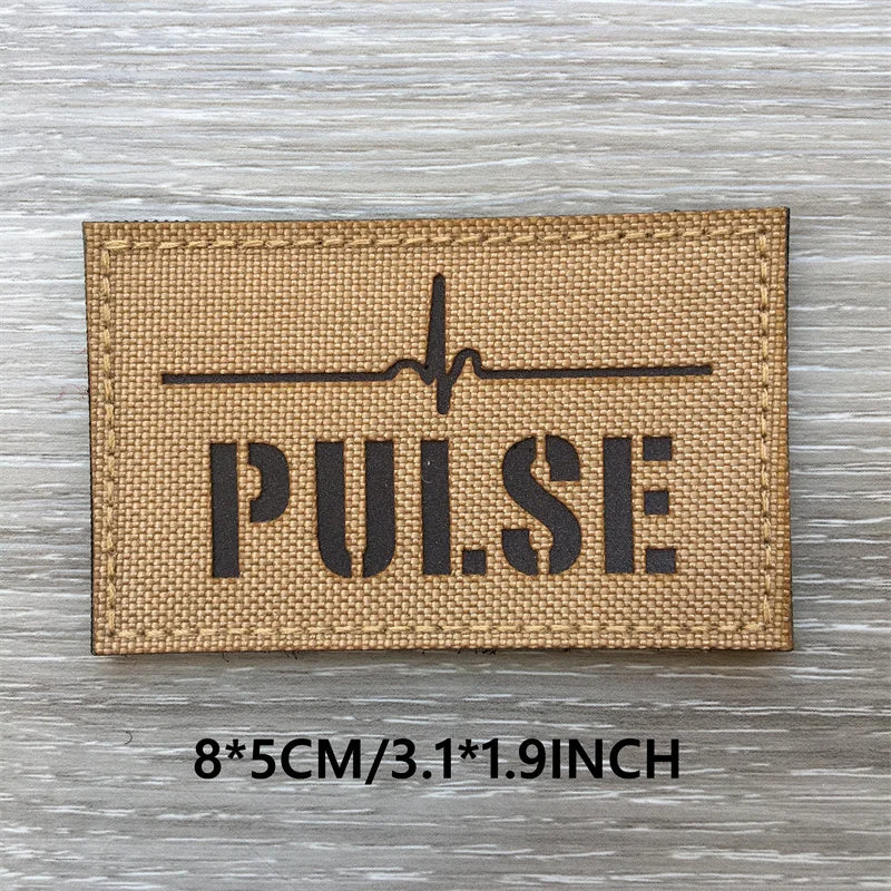A tan fabric patch with the word PULSE and a heartbeat line printed on it, set against a light wooden background.