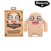 A beige knitted plush toy of an ugly monster with large eyes and pink teeth, packaged in a brown box.