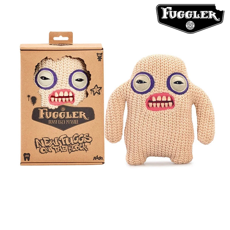 A beige knitted plush toy of an ugly monster with large eyes and pink teeth, packaged in a brown box.