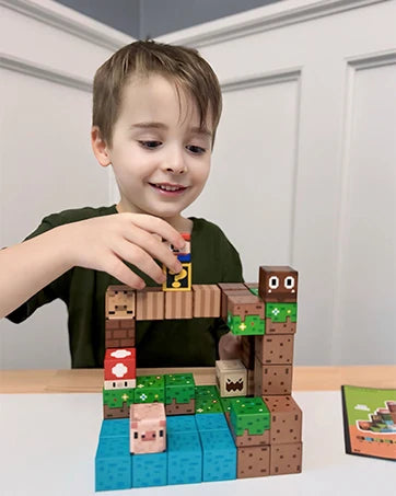 A young boy is building a wooden magnetic block house structure with other blocks on a white table.
