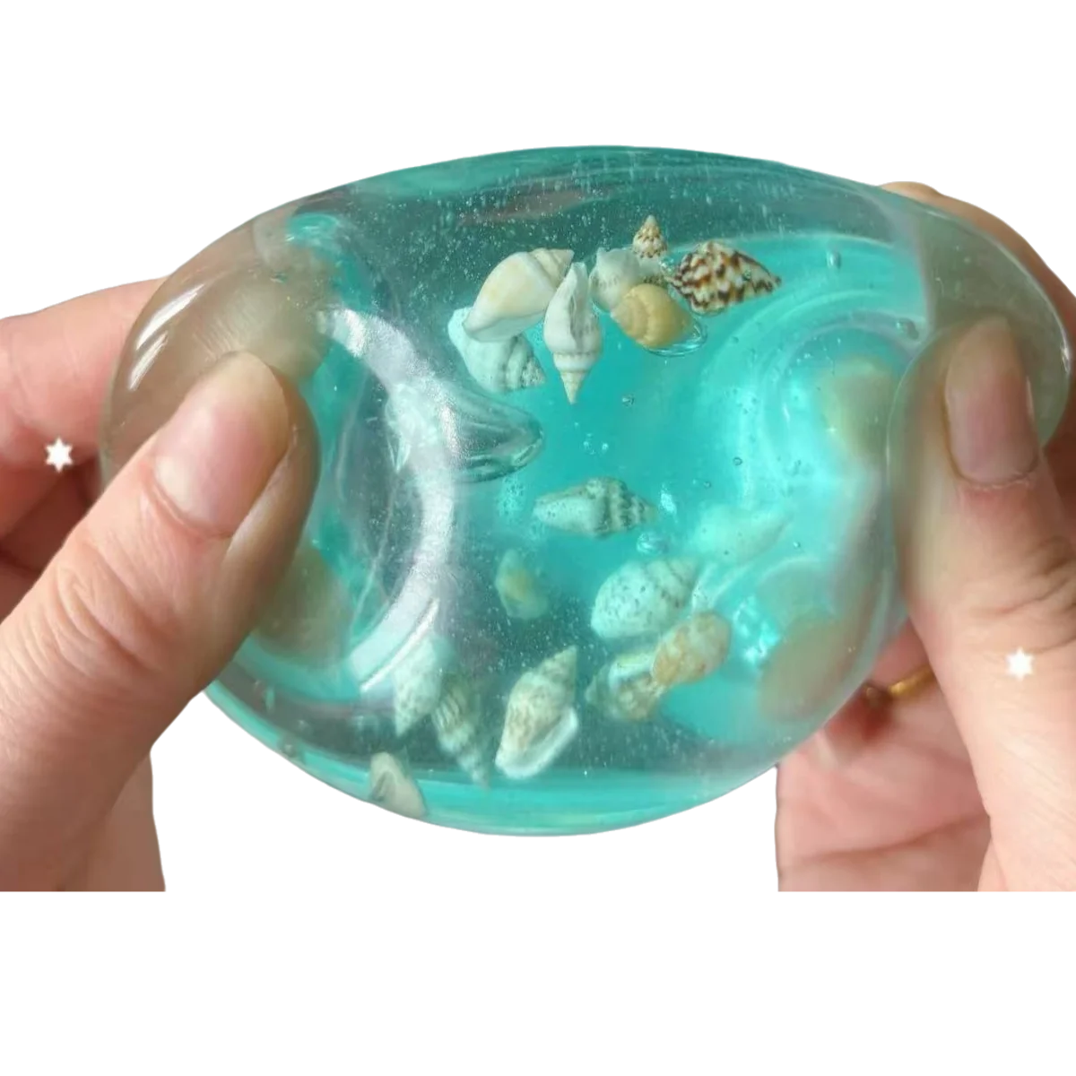 A hand holds a translucent blue liquid containing small seashells and sea creatures, used for sensory play.
