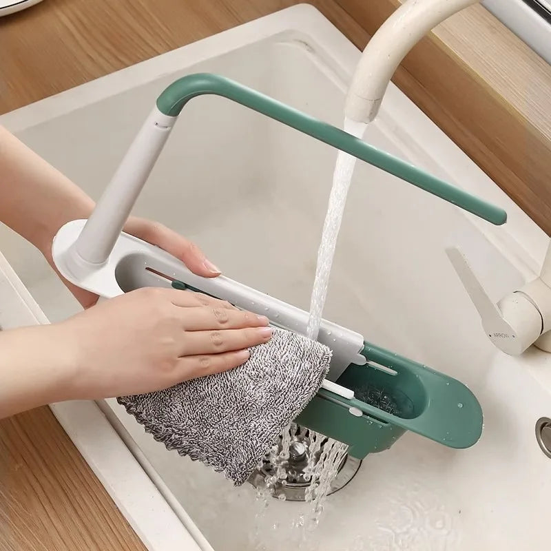 A hand is using an adjustable over-sink dish drying rack to wash dishes in a kitchen sink.