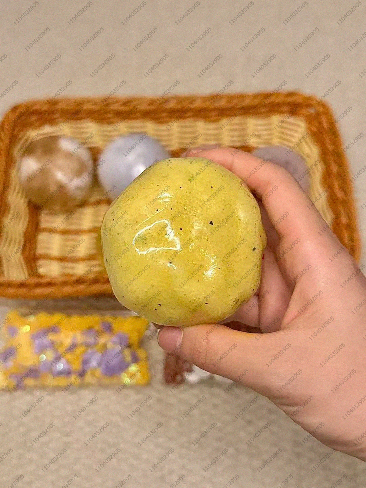 Eine Hand hält einen leuchtend gelben, glatten Stressball neben anderen bunten Bällen in einer Holzschale.