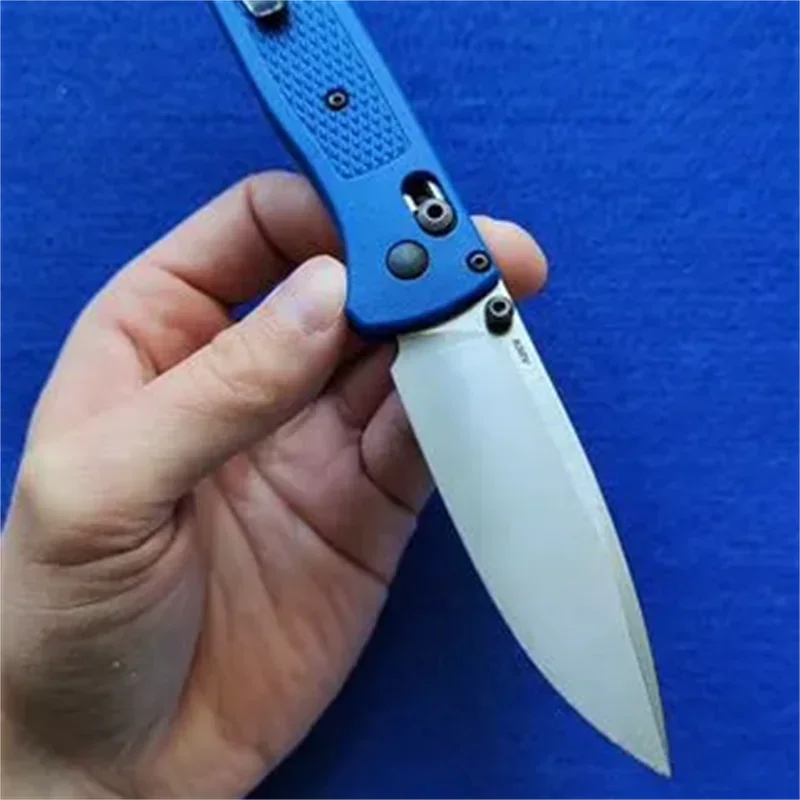 A hand holds a blue CPM-20CV folding pocket knife with a drop point blade against a blue background.