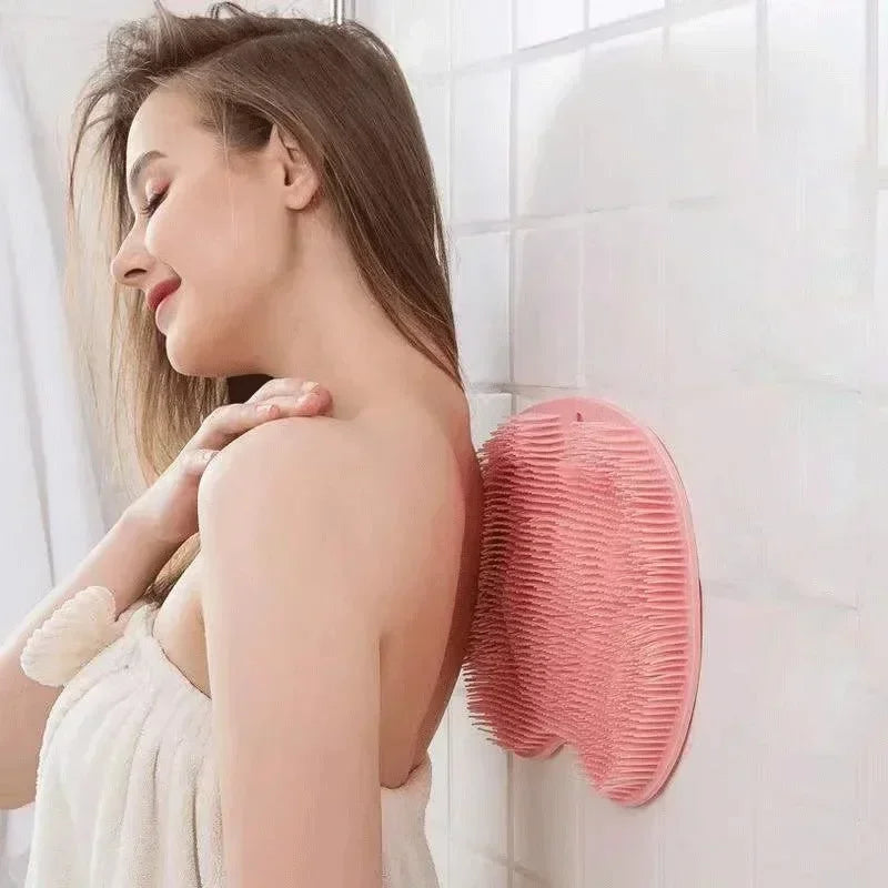 A woman is using a pink silicone exfoliating shower mat on her shoulder while in a bathroom setting.