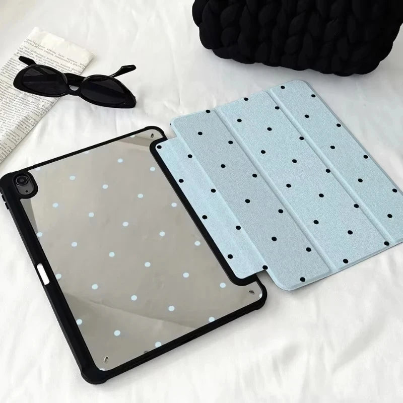 Helles blaues Schutzhülle mit dekorativen Bleistift-Fächern für ein iPad, neben Sonnenbrille und schwarzem Stoff.
