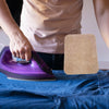 A hand is ironing fabric on a blue cloth using a purple heat-resistant wool felt ironing mat.