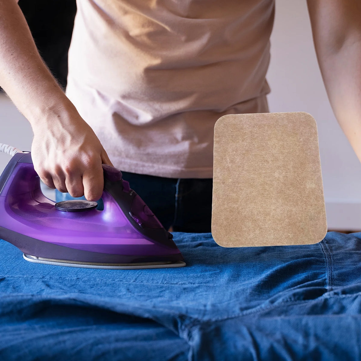 A hand is ironing fabric on a blue cloth using a purple heat-resistant wool felt ironing mat.