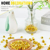 Gold acrylic crushed ice gems scattered on a white surface next to a glass vase and a ceramic bird.
