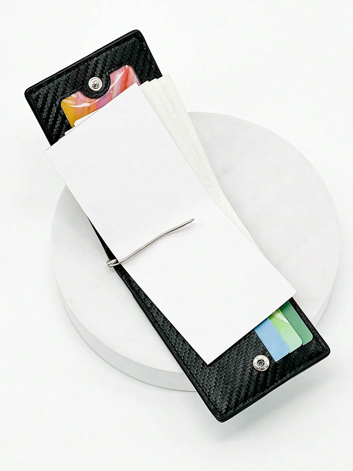 Schwarzes Kohlefaser-Kartenträger-Wallet mit weißer Karte und farbenfrohen Karten darin, auf einer weißen Oberfläche.