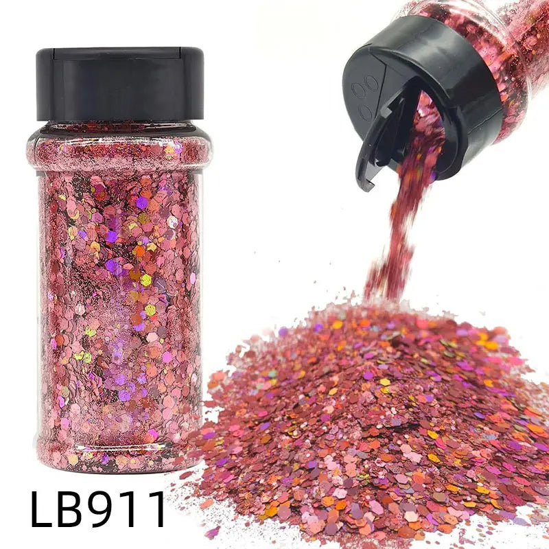 A glass jar of holographic chunky nail glitter mix with a black shaker top next to a pile of the same pink glitter.