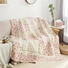 A pink and cream floral patchwork quilt with embroidery draped over a sofa.