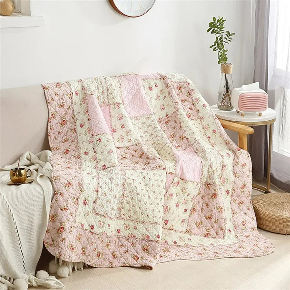 A pink and cream floral patchwork quilt with embroidery draped over a sofa.