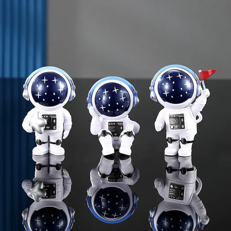 Three handcrafted astronaut figurines in white and blue resin displayed on a reflective surface.